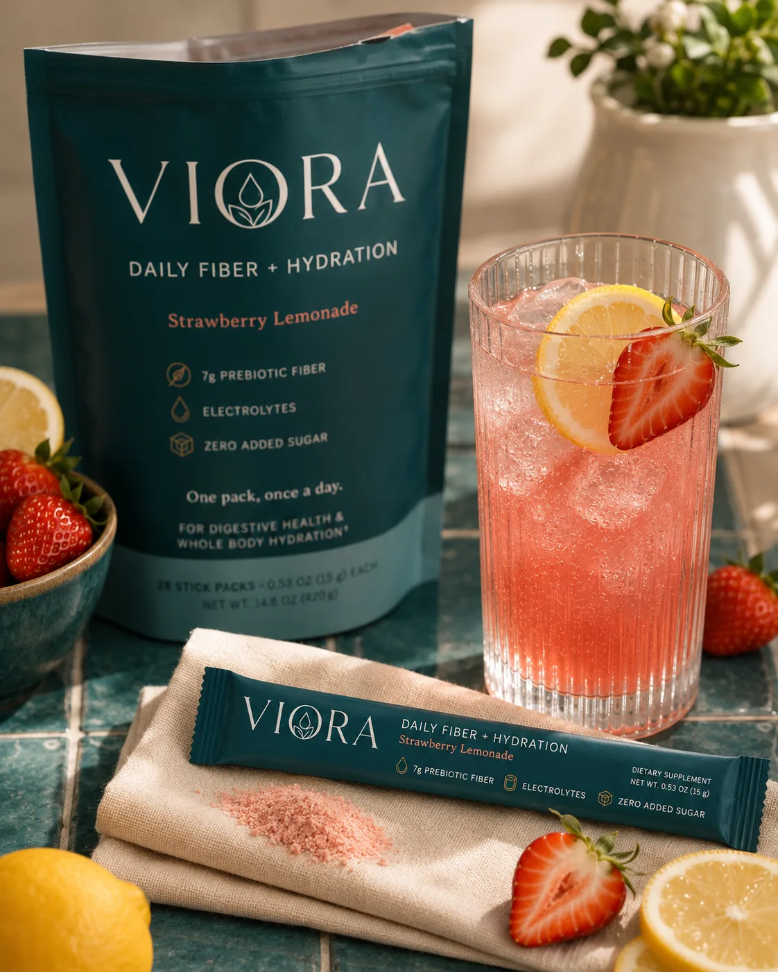 A single Viora stick pack on folded linen beside a just-stirred glass of strawberry lemonade